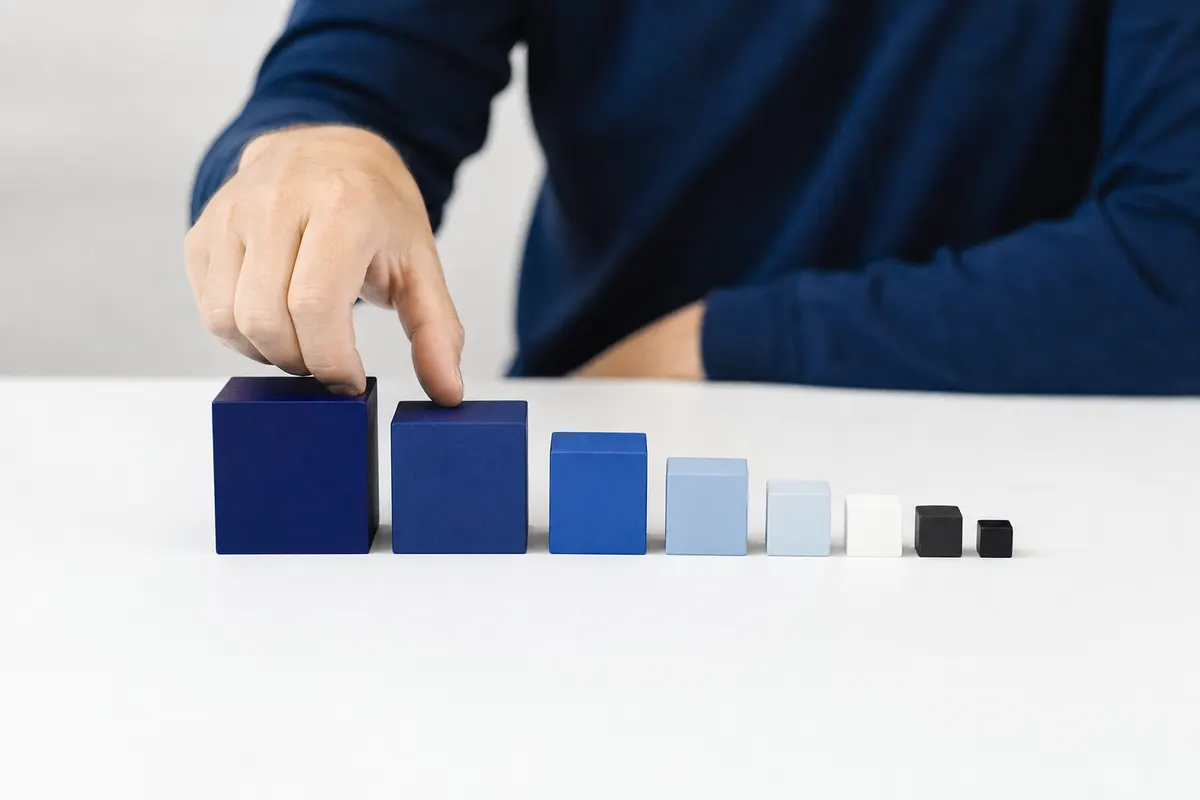 Uma mão organizando blocos de madeira coloridos em ordem decrescente de tamanho.